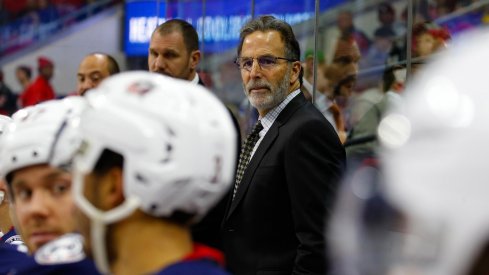 John Tortorella looks thoughtfully off the bench at his players.