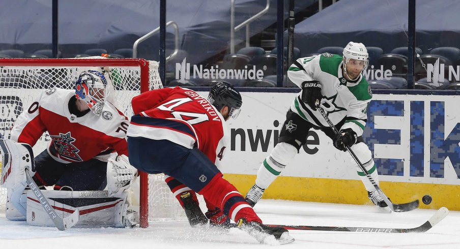 Feb 2, 2021; Columbus, Ohio, USA; Dallas Stars center Andrew Cogliano (11) passes the puck over the outstretched stick of Columbus Blue Jackets defenseman Vladislav Gavrikov (44) during the second period at Nationwide Arena.