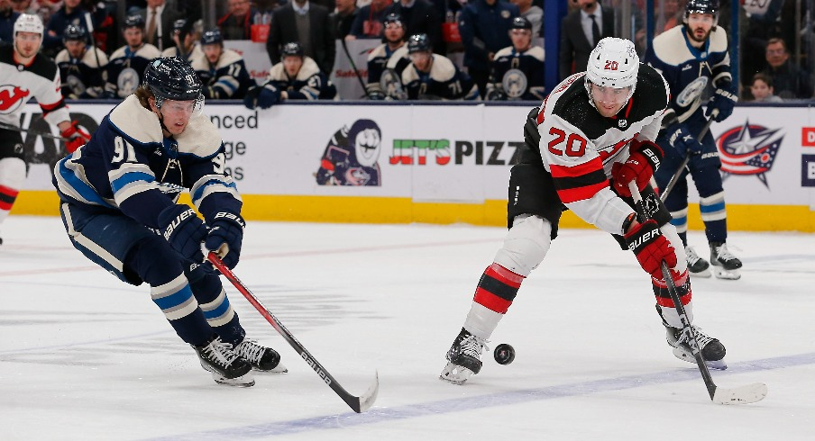 New Jersey Devils center Michael McLeod (20) passes the puck over the stick of Columbus Blue Jackets left wing Kent Johnson (91) during the second period at Nationwide Arena.